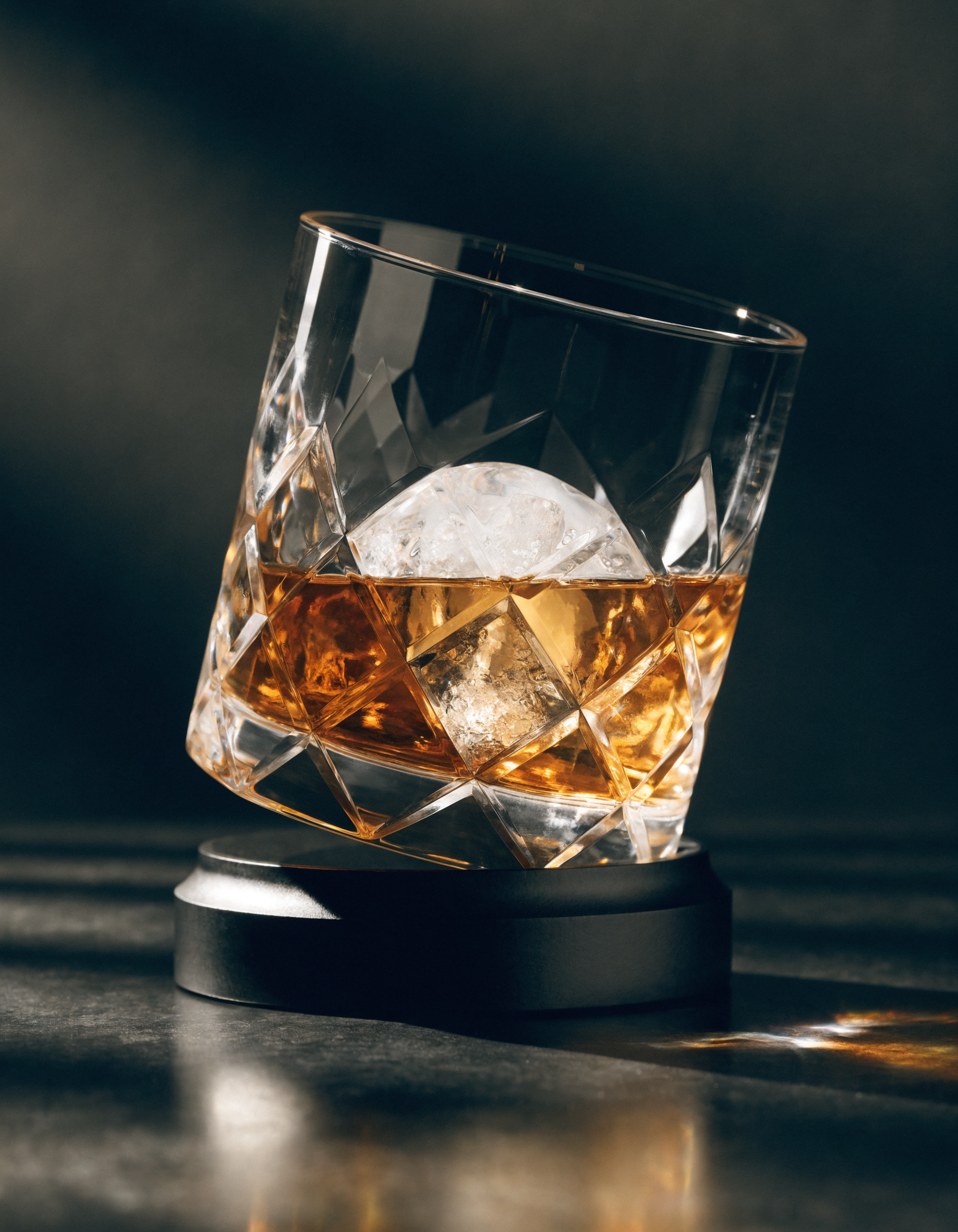 The Oember Vortex gemstone-cut rotating whiskey glass with amber whiskey and ice, dark luxury product shot