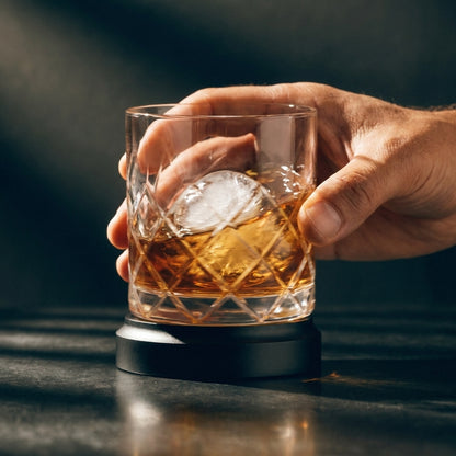 A hand spinning the Oember Vortex whiskey glass on its kinetic rotating base